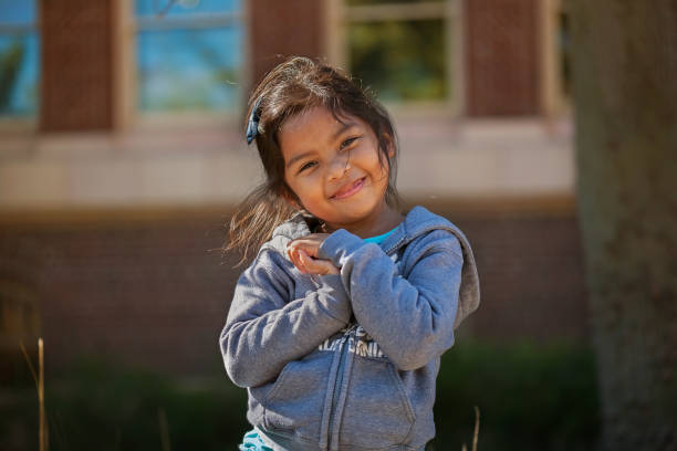 linda niña sosteniendo sus manos juntas que está expresando amor, felicidad o sonrisa, con un edificio escolar hecho de ladrillos de fondo. - 4 5 años fotografías e imágenes de stock