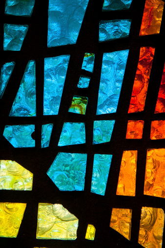 Detail of a multicolored mosaic of translucent colors in the stained glass of a church window.