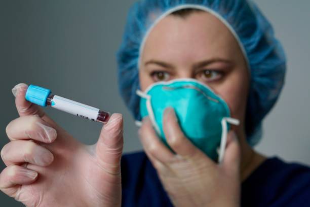 Nurse with a respirator mask holds out a blood specimen with a blank label stock photo
