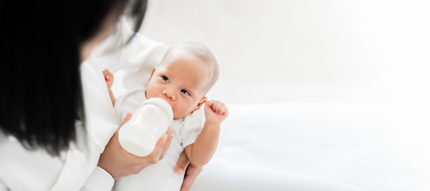 Madre alimentando bebé asiático con biberón de leche, espacio de copia de pancarta photo