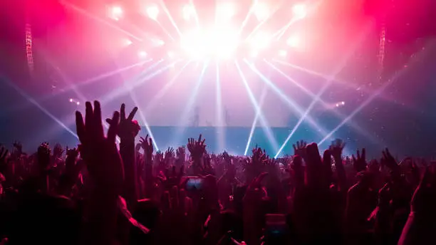 Happy people dance in nightclub DJ party concert and listen to electronic dancing music from DJ on the stage. Silhouette cheerful crowd celebrate New Year party 2020. People lifestyle DJ nightlife.