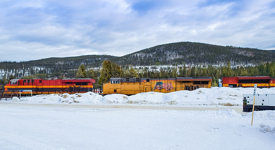 View of freight train traveling through western Colorado in winter; snow in foreground and mountains in background