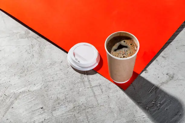 Fresh hot coffee in disposable cup on a red and a concrete backgrounds