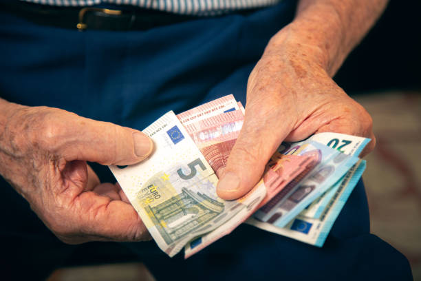 istock Old man sitting at home counting her money 1201095088
