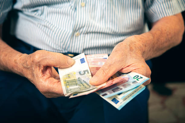 istock Old man sitting at home counting her money 1201095138