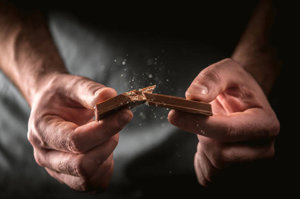 Man breaks a chocolate bar Man breaks a chocolate bar on dark background man hand holding candy bar stock pictures, royalty-free photos & images