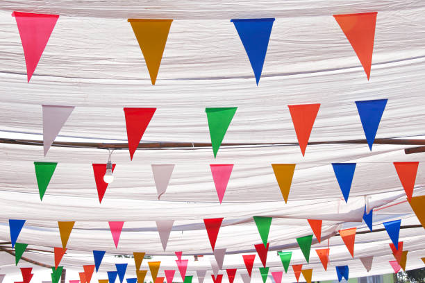 istock Multicolored colorful triangles bunting paper cut hanging on white thread under fabric roof at street night market 1201105453