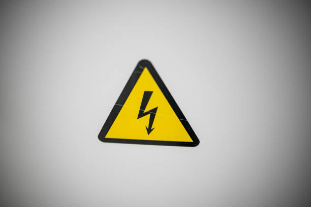Sign danger high voltage. Sign dangerously high voltage electricity. A yellow triangle mark with a lightning bolt in the center. This warning is painted on an old metal surface painted with gray paint