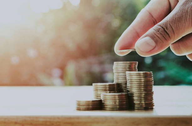 istock saving money hand putting coins on stack on table with sunshine. concept finance and 1201112260