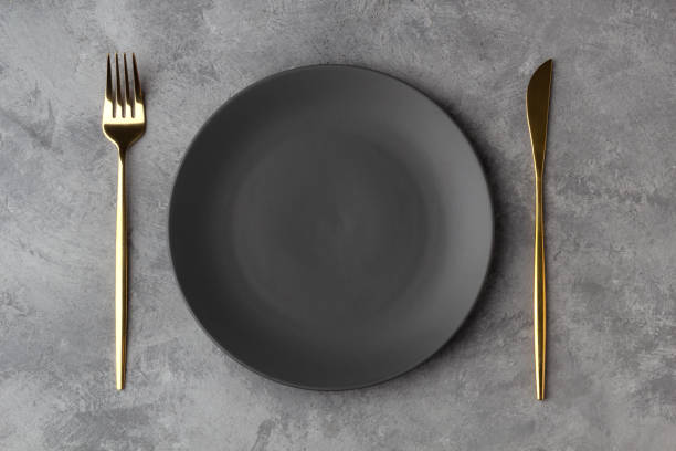istock Empty gray plate with a gold knife and fork on a gray concrete background 1201114944