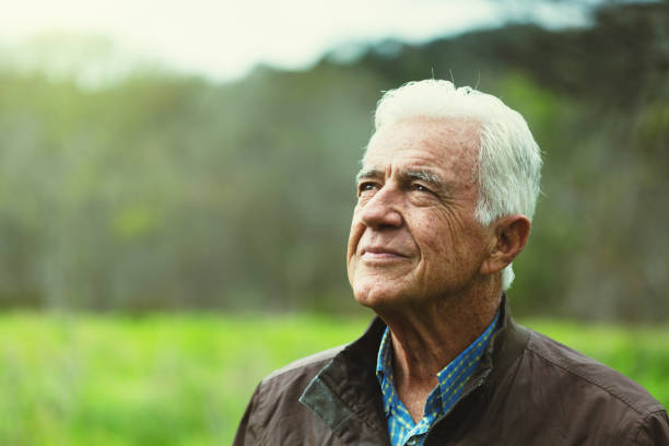Smiling gently, a senior man walking outdoors looks upwards