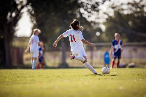 vista posteriore di una determinata giocatrice di calcio femminile che calcia la palla in una partita. - hit and run foto e immagini stock