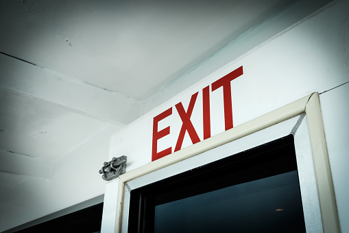 A close-up red exit directional sign, painted on the white door on a yacht
