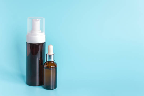 istock Small brown dropper bottle and big bottle with white dispenser on blue background. Concept beauty cosmetics product 1201126983