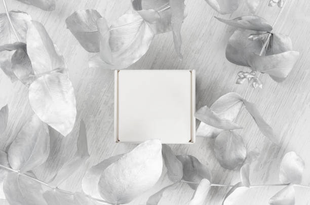istock Elegant white blank closed paper square gift box mock up on wood board with silver branch, leaves top view for design, branding identity, advertising. 1201139327