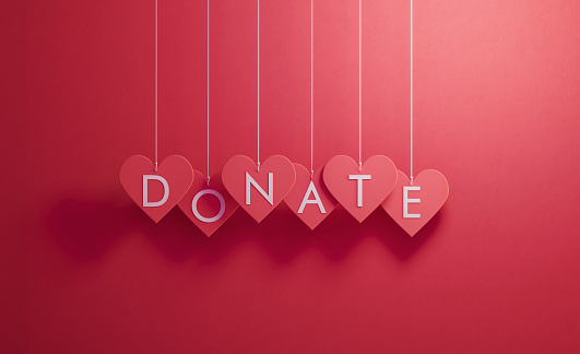 Donate writes over red heart shapes hanging over red background, Horizontal composition. Donation concept.