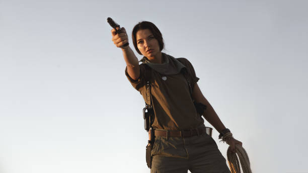 istock Woman Standing With a Gun Outdoors in Desert 1201143678