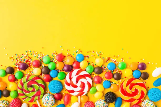 Colorful candies over yellow background. Top view. Flat lay. Copy space. Sweet mix for birthday or candy shop