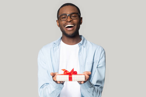 szczęśliwy afroamerykanin prezentuje pudełko z kokardką - box men holding isolated zdjęcia i obrazy z banku zdjęć
