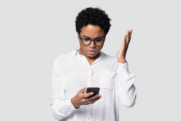 Confused biracial woman have malfunction problem using cellphone Confused african American millennial woman isolated on grey studio background hold smartphone have problem with gadget, frustrated biracial female experience cellphone malfunction or virus attack poor signal stock pictures, royalty-free photos & images