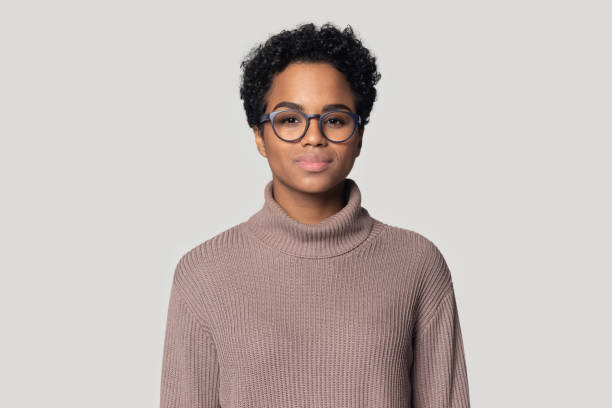 Headshot of black woman in glasses posing isolated in studio Headshot portrait of beautiful african American millennial woman in glasses and sweater stand isolated on grey studio background, black biracial female wearing spectacles look at camera posing serious black teen stock pictures, royalty-free photos & images