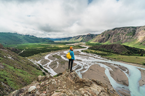 Young Caucasian woman standing and looking at river  in Patagonian Andes in Argentina