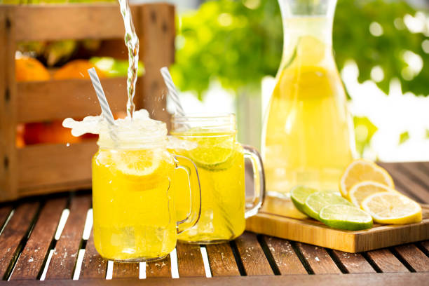 enchendo limonada fresca em copo de jarra de pedreiro na mesa de madeira do lado de fora - pouring water carafe glass - fotografias e filmes do acervo