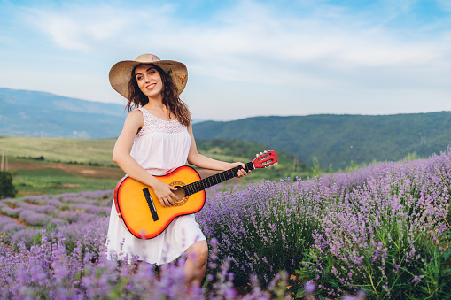 Young caucasian beautiful woman playing guitar in lavender field.
