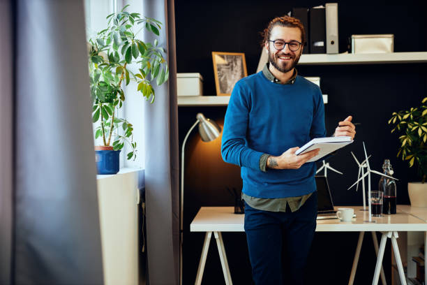 jeune caucasien caucasien souriant concepteur graphique créateur et innovateur restant dans son bureau et écrivant des idées dans le cahier. - directeur de la création photos et images de collection