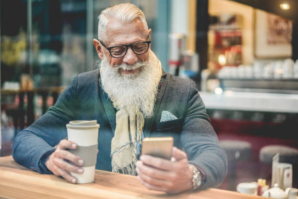 istock Senior business man using smartphone app while drinking coffee inside cafe bar - Trendy entrepreneur doing breakfast - Job, morning break and tech concept - Window from outside view - Focus on face 1201154683