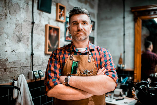 istock A barber with twirled mustache and an apron posing for camera in a barber shop 1201156649