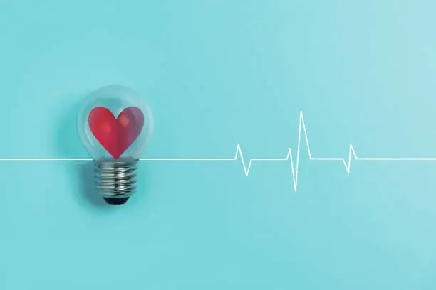 Photo of Red heart in light bulb with Heartbeat pulse on blue background.