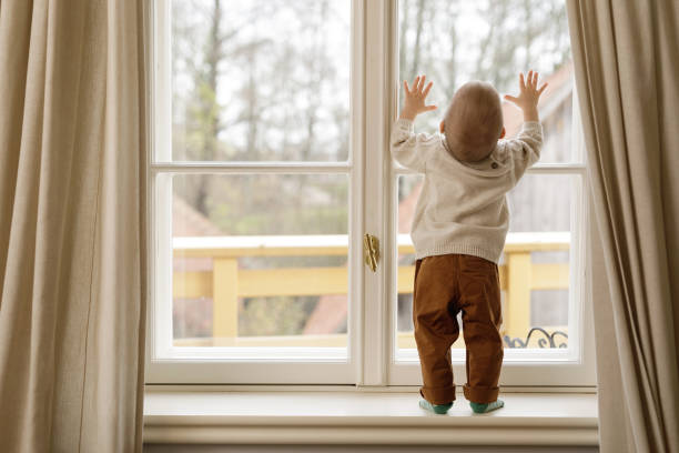 istock Baby boy is standing on the windowsill and looking at the window 1201159677