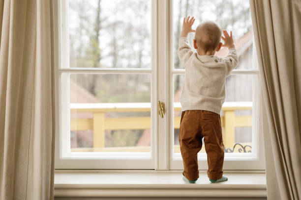 istock Baby boy is standing on the windowsill and looking at the window 1201159705
