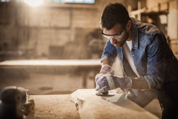 Male manual worker using plane while working on a wood in a workshop. Young manual worker working with plane on a piece of wood in workshop. plane hand tool photos stock pictures, royalty-free photos & images