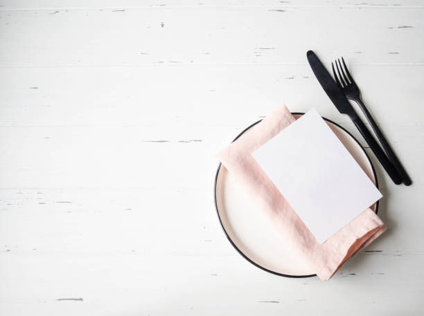 istock Rustic table setting with plate, pink napkin, card and appliances on white wood table. Top view. 1201160301