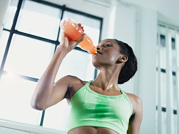 African American woman drinking an energy drink at the gym young african american woman in sportswear with energy drink in gym. Horizontal shape, waist up, low angle view sport drink stock pictures, royalty-free photos & images