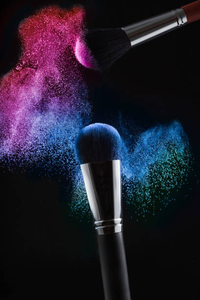 escovas para uma maquiagem em um fundo preto com pó rosa e azul espirram de perto. - face powder exploding make up dust - fotografias e filmes do acervo