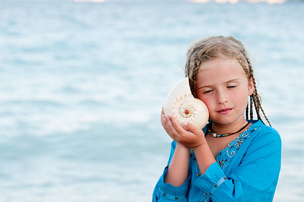 Young girl with a conch shell to her ear listening to sea stock photo