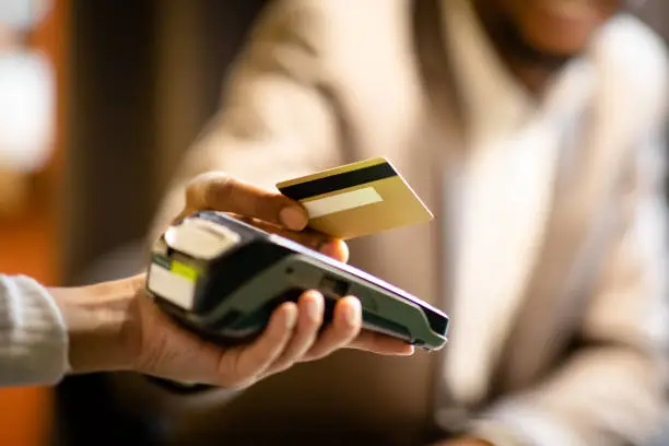 Unrecognizable afro businessman in suit giving credit card to barman paying with gold credit card in cafe, close up