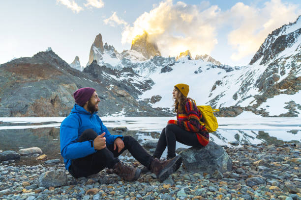 hombre y mujer sentados cerca del lago en el fondo de la montaña fitz roy en la patagonia - turismo argentina fotografías e imágenes de stock