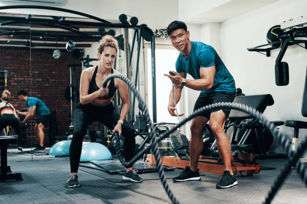 You can do this! Cropped shot of an attractive young sportswoman working out with battle ropes with her personal trainer in a gym extreme dedication stock pictures, royalty-free photos & images