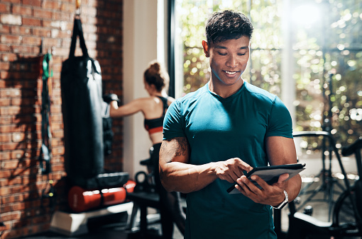 Cropped shot of a handsome young sportsman using a digital tablet in a gym with his fitness partner in the background