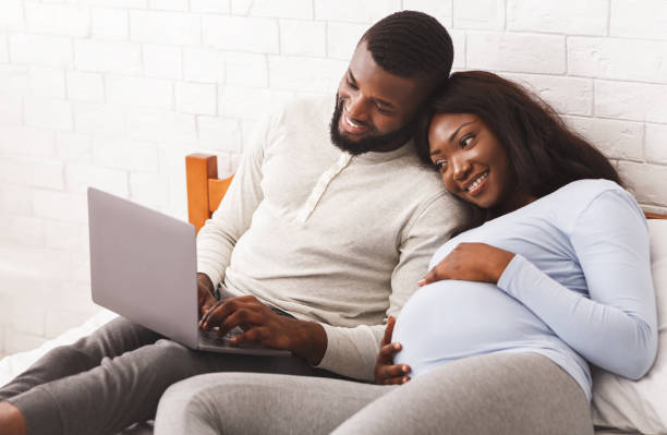 прекрасная беременная пара с помощью ноутбука во время отдыха - human pregnancy african ethnicity women family стоковые фото и изображения