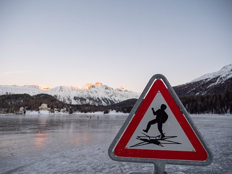 Frozen lake and snowcapped mountain in Switzerland, Danger sign for walking on thin ice