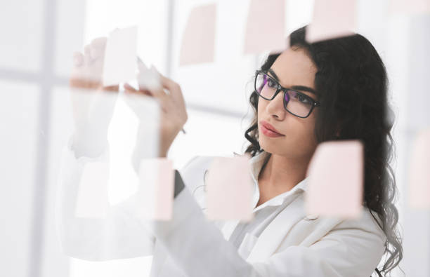 istock Hispanic manager writing on adhesive notes on glass wall 1201177373