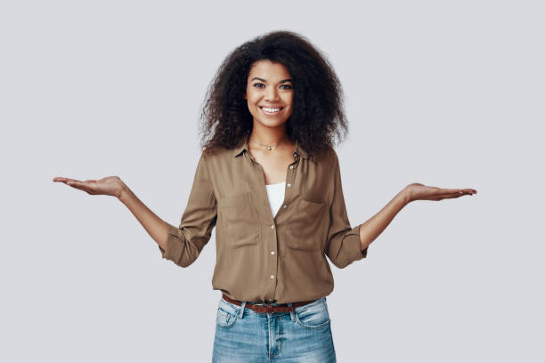 istock Confident young African woman pointing copy space and smiling while standing against grey background 1201179005