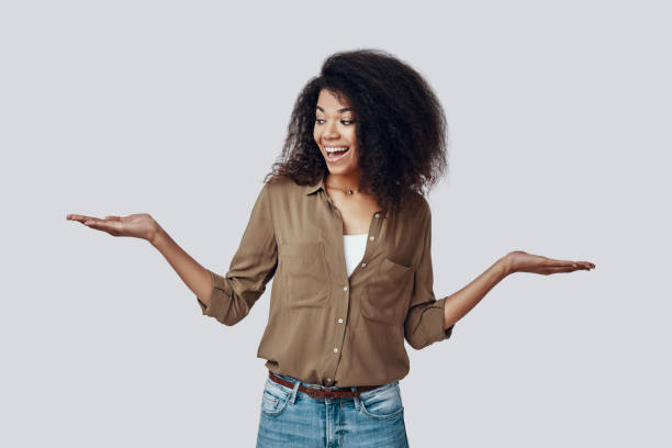 istock Beautiful young African woman pointing copy space and smiling while standing against grey background 1201179052