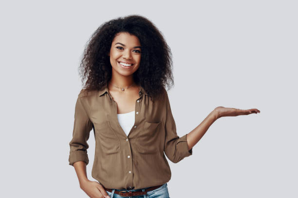 istock Beautiful young African woman pointing copy space and smiling while standing against grey background 1201179125