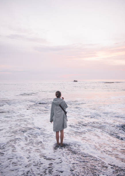 Rear view of young barefoot woman standing in water at beach.